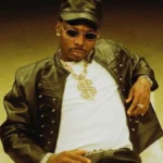 Asake photographed in a studded leather jacket and cap against a warm gold backdrop