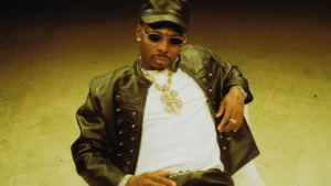 Asake photographed in a studded leather jacket and cap against a warm gold backdrop