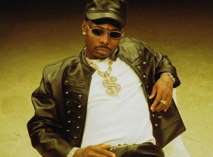 Asake photographed in a studded leather jacket and cap against a warm gold backdrop