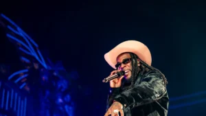 Burna Boy performing on stage in a wide-brimmed hat holding a microphone