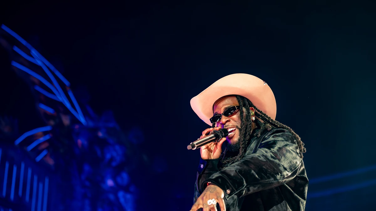 Burna Boy performing on stage in a wide-brimmed hat holding a microphone